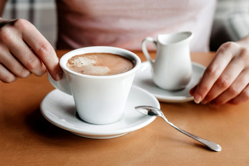 Morning coffee. Closeup of women's hands with coffee cup in a cafe. Female hands holding cups of coffee on a wooden table background in a cafe, vintage color tone