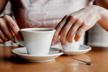 Fototapeta na wymiar Morning coffee. Closeup of women's hands with coffee cup in a cafe. Female hands holding cups of coffee on a wooden table background in a cafe, vintage color tone