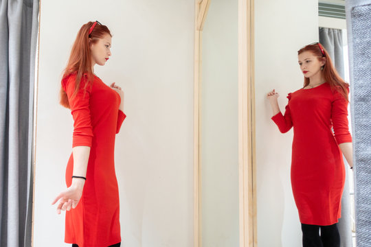 pretty woman trying on clothes in a fitting shop. the lady in the red dress is reflected in the mirror.