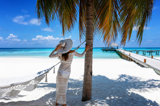 Attraktive Reisende in wei&szlig;em Sommerkleid steht unter einer Palme am tropischen Strand der Malediven