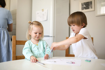 Children siblings paint at table in white kitchen