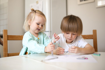 Fototapeta premium Children siblings paint at table in white kitchen