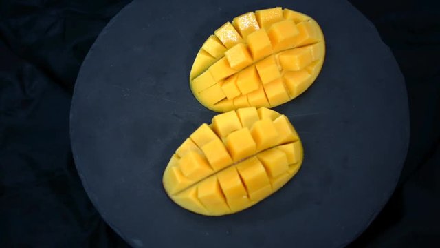 Organic tropical fruits, close up slides mangoes on black plate.