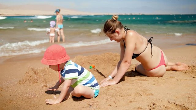 4k video of little toddler boy playing with his mother on ea beach. FAmily playing toys and relaxing on summer vacation