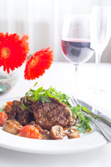 The concept of Italian cuisine. Juicy steak of beef aging stewed meat, with rucola salad and cherry tomatoes. A glass of red wine and bread basket on the table