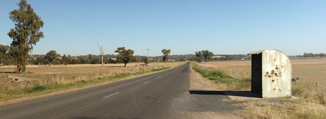 Fototapeta premium lone rural rustic rusty farm covered school bus station stop on a long empty sealed road in a cattle farming district, rural New South Wales, Australia