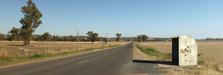 Obraz premium lone rural rustic rusty farm covered school bus station stop on a long empty sealed road in a cattle farming district, rural New South Wales, Australia