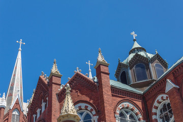 Fototapeta premium Ornate spires, domes, and windows of a Gothic Revival church featuring three white crosses against blue sky, horizontal aspect