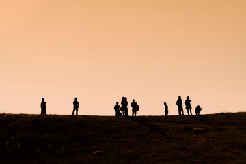 Fototapeta na wymiar Silhouettes of hikers with backpacks enjoying sunset view from top of a mountain