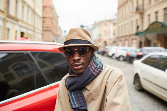Portrait of fashionable African man wearing hat and trenchcoat posing outdoors in city