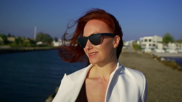 closeup portrait of beautiful European cute redhead in sunglasses young woman or a girl who's fun, the wind is blowing hair in the wind, slow motion