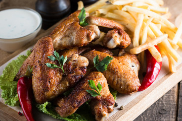 Close-up photo of bbq chicken wings with fries and beer. Barbeques meat with sauces, ketchup, mayonnaise. Fast and junk food concept. 