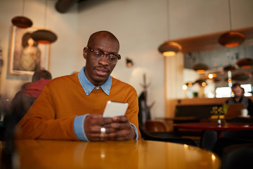 Warm toned portrait of contemporary African man using smartphone  sitting at table in cafe, copy space