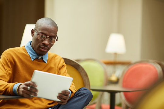 Portrait of contemporary African man using digital tablet sitting outdoors at table in cafe, copy space