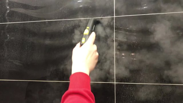 Cleaning the black ceramic tile with a steam cleaner in the bathroom. A person does the cleaning with hot water; a steam jet removes pressure dirt from the joints. The work of cleaning services