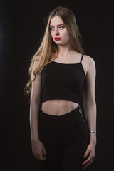 Young beautiful, slender, passionate brown-haired woman with bright red lips and long hair in a black top and denim shorts on a dark background