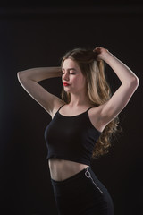 Fototapeta premium Young beautiful, slender, passionate brown-haired woman with bright red lips and long hair in a black top and denim shorts on a dark background