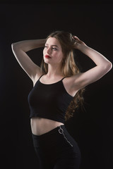 Fototapeta na wymiar Young beautiful, slender, passionate brown-haired woman with bright red lips and long hair in a black top and denim shorts on a dark background