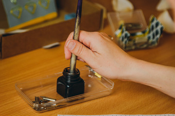 female hand dipping ink pen into inkwell. stationery on wooden desk close up. spelling lessons and caligraphy exercises