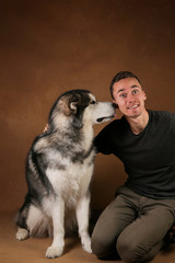 Studo shot of a man and alaskan malamute dog stitting on brown blackground