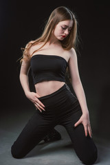 Obraz na płótnie Canvas Young beautiful, slender, passionate brown-haired woman with bright red lips and long hair in a black top and denim shorts on a dark background