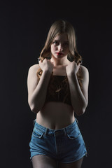 Fototapeta premium Young beautiful, slender, passionate brown-haired woman with bright red lips and long hair in a black top and denim shorts on a dark background