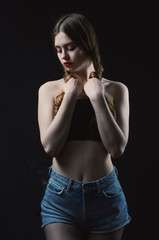 Naklejka premium Young beautiful, slender, passionate brown-haired woman with bright red lips and long hair in a black top and denim shorts on a dark background