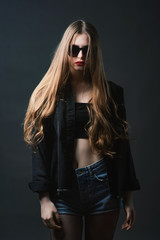 Young beautiful, slender, passionate brown-haired woman with bright red lips and long hair in a black top and denim shorts on a dark background