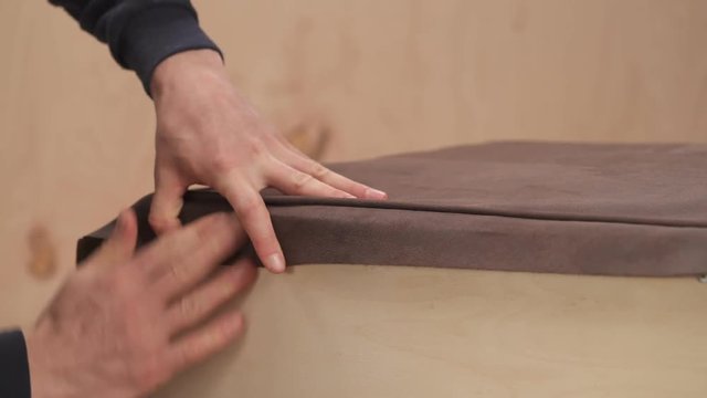 Highly professional worker is wrapping a sofa with a cloth. He is fixing fabric with industrial stapling machine in a workshop of factory