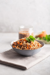 Boiled buckwheat cereal with carrot, parsley and butter in a bowl on a gray background. Traditional Russian dish on gray background with copy space