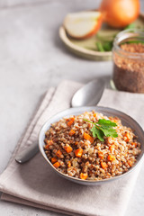 Boiled buckwheat cereal with carrot, parsley and butter in a bowl on a gray background. Traditional Russian dish on gray background with copy space