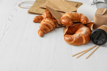 Paper bags with pastry and takeaway food on light table. Space for text