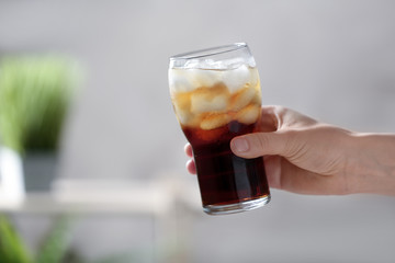 Woman holding glass of cola with ice on blurred background, closeup. Space for text