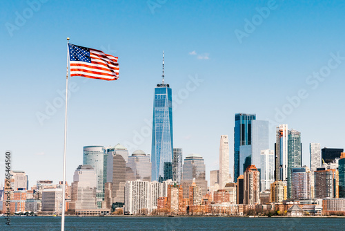 American national flag on sunny day with New York city Manhattan island in background. America cityscape, or United States nation symbol concept