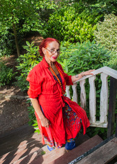 Modern unusual senior oriental woman in red dress walking up the wooden steps.