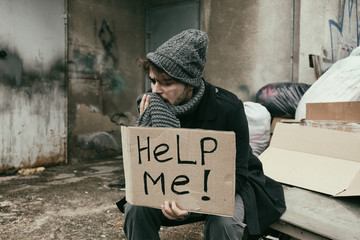Poor young man with HELP ME sign at dump