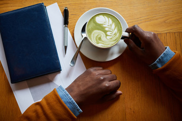 Top view closeup of contemporary African-American man drinking latte while sitting at table in coffee shop, copy space