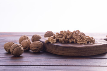 Cracked and whole walnuts lying on cutting board and wooden table, side view on white background. Healthy nuts and seeds composition.