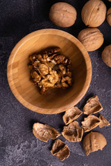Cracked walnuts in wooden bowl and on black slate surface. Healthy nuts and seeds composition.