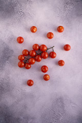 Bunch of cherry tomatoes on white textured stone concrete table, top view with copy space. Ingredients for cooking.
