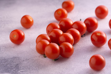 Bunch of cherry tomatoes on white textured stone concrete table, side view with copy space. Ingredients for cooking.