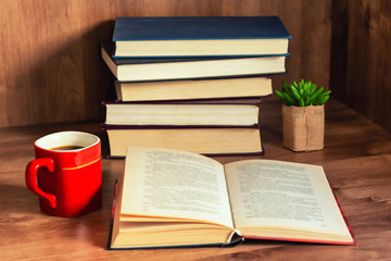 Pile of closed books and open book with cup of coffee on wooden background.