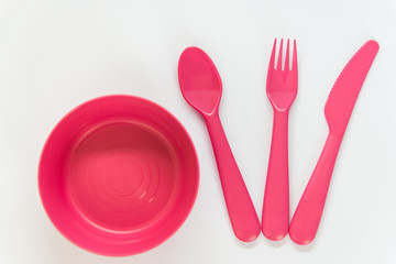 Pink spoon, fork, knife and plate on the white background.