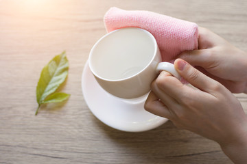 Close up woman hand cleaning coffee cup on the morning with microfiber cloth,Close up woman hand cleaning coffee cup on the rustic wood table.