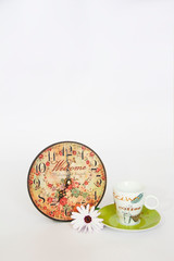 Obraz na płótnie Canvas coffee pot on a green saucer, decorative patterned clock and white daisy flower on a white background