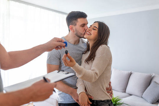 Happy young couple getting keys of their new home. View of Real estate agent delivers keys of new house to young couple. New house / home moving and relocation concept