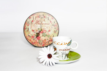 Obraz na płótnie Canvas coffee pot on a green saucer, decorative patterned clock and white daisy flower on a white background