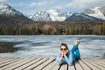 A woman in jeans lying by frozen mountains lake Strbske pleso.