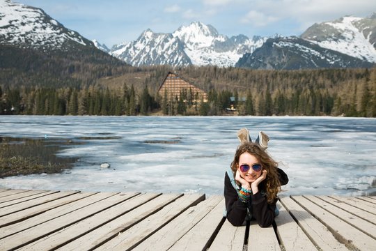 Young girl is lying on wooden terrace by frozen mountains lake S