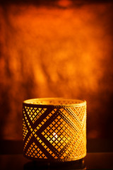 Fototapeta na wymiar Decorative eastern textured candlestick with burning candle, glowing at night and with glittering golden bokeh lights. Festive greeting card, invitation for the Muslim holy month of Ramadan Hareem. 